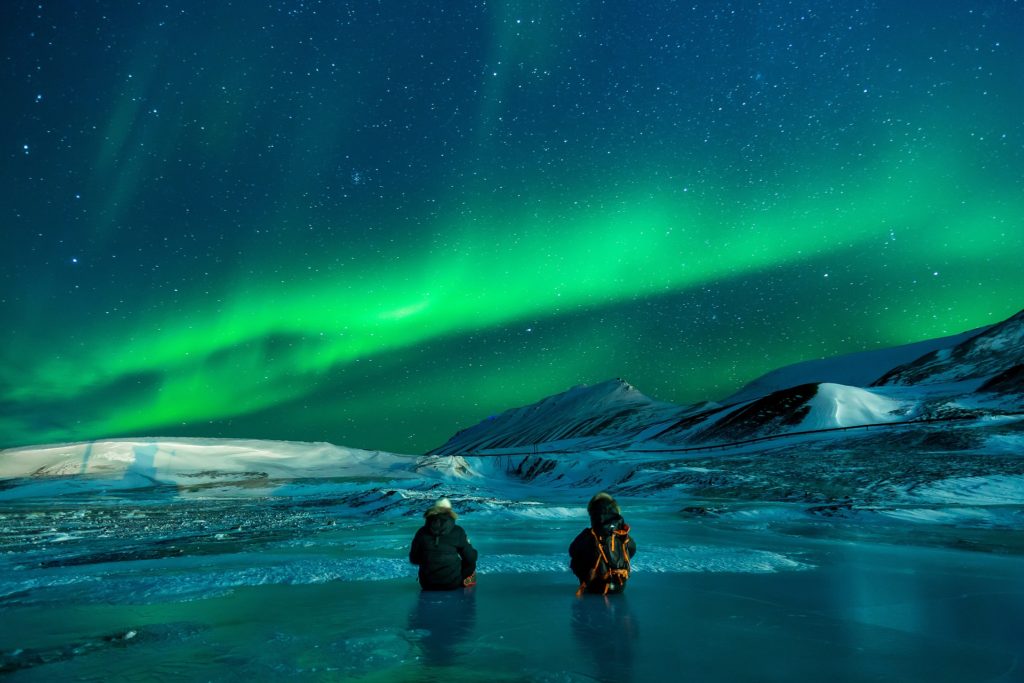 Dvoje ljudi sjedi na zaleđenom jezeru i promatra polarnu svjetlost